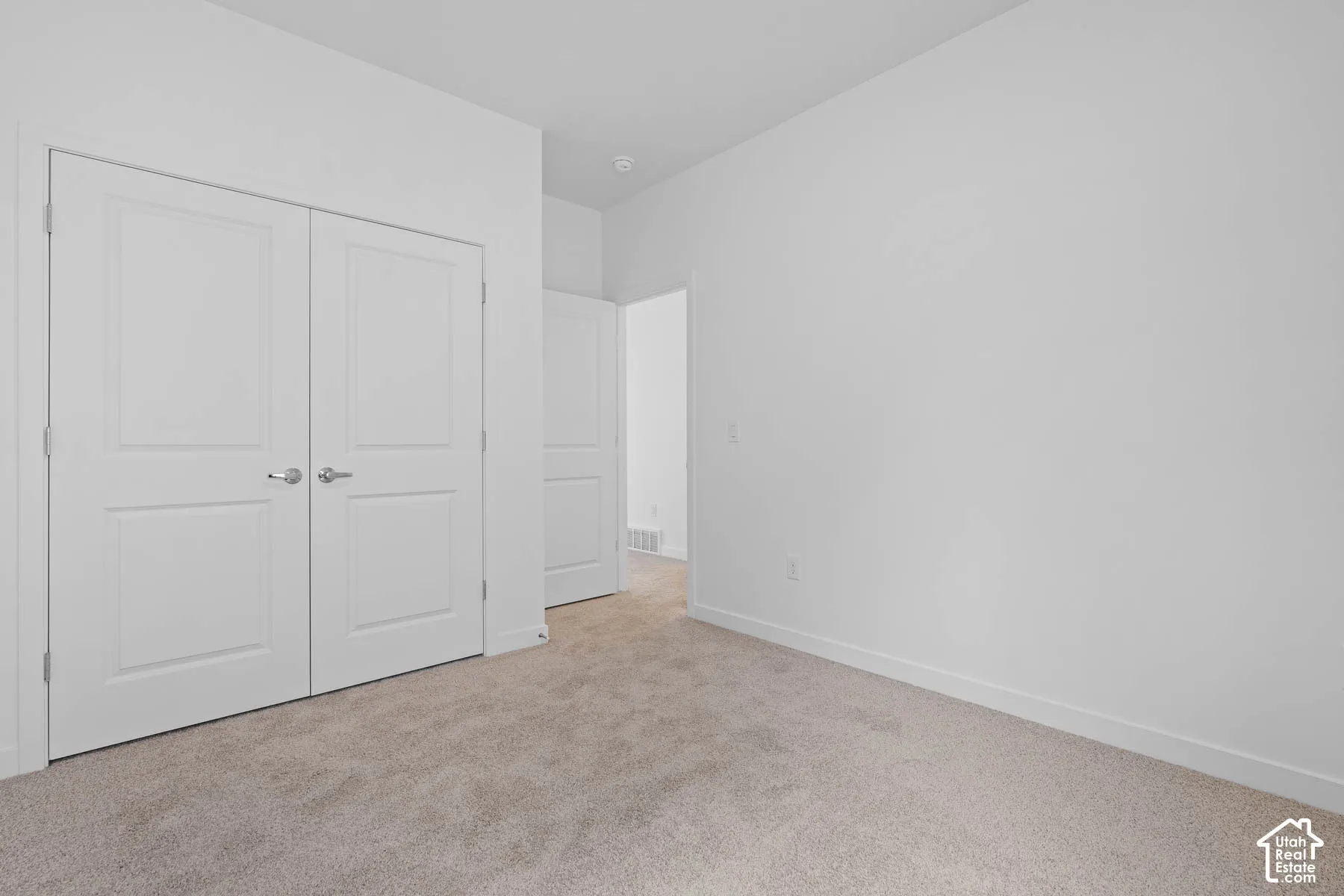 Neutral tone wall finish, light-colored carpeting, white trim, and double panel doors