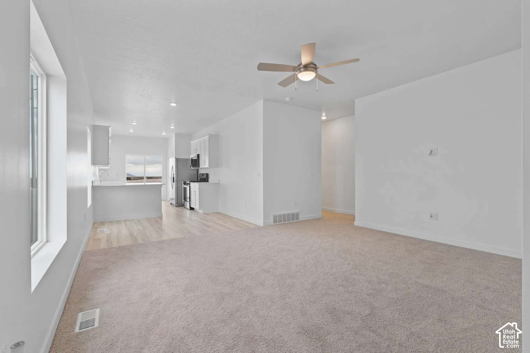 Open-concept living area with neutral carpeting, wood-finish flooring, and recessed lighting