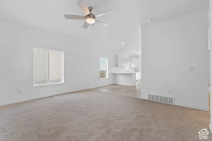 Expansive living area featuring light-toned carpeting and a ceiling fan with integrated lighting