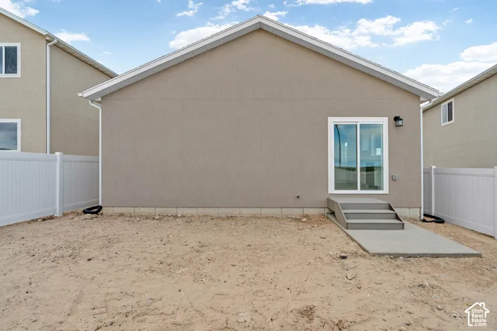 Stucco exterior with white trim, featuring a sliding glass door and concrete steps leading to a concrete patio