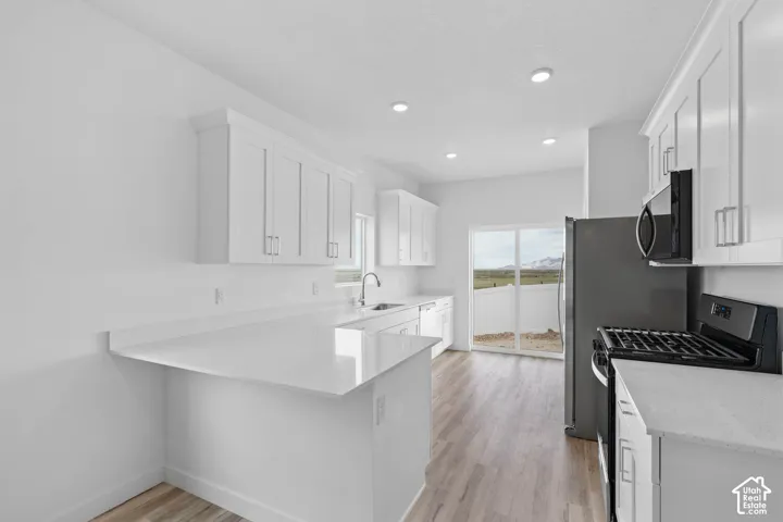 White shaker cabinetry, light-toned wood-finish flooring, recessed lighting, and a stainless steel sink with a gooseneck faucet