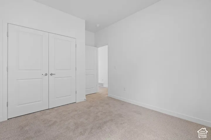 Neutral tone wall finish, light-colored carpeting, white trim, and double panel doors