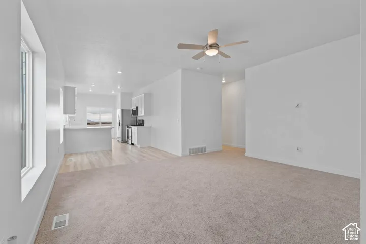 Open-concept living area with neutral carpeting, wood-finish flooring, and recessed lighting