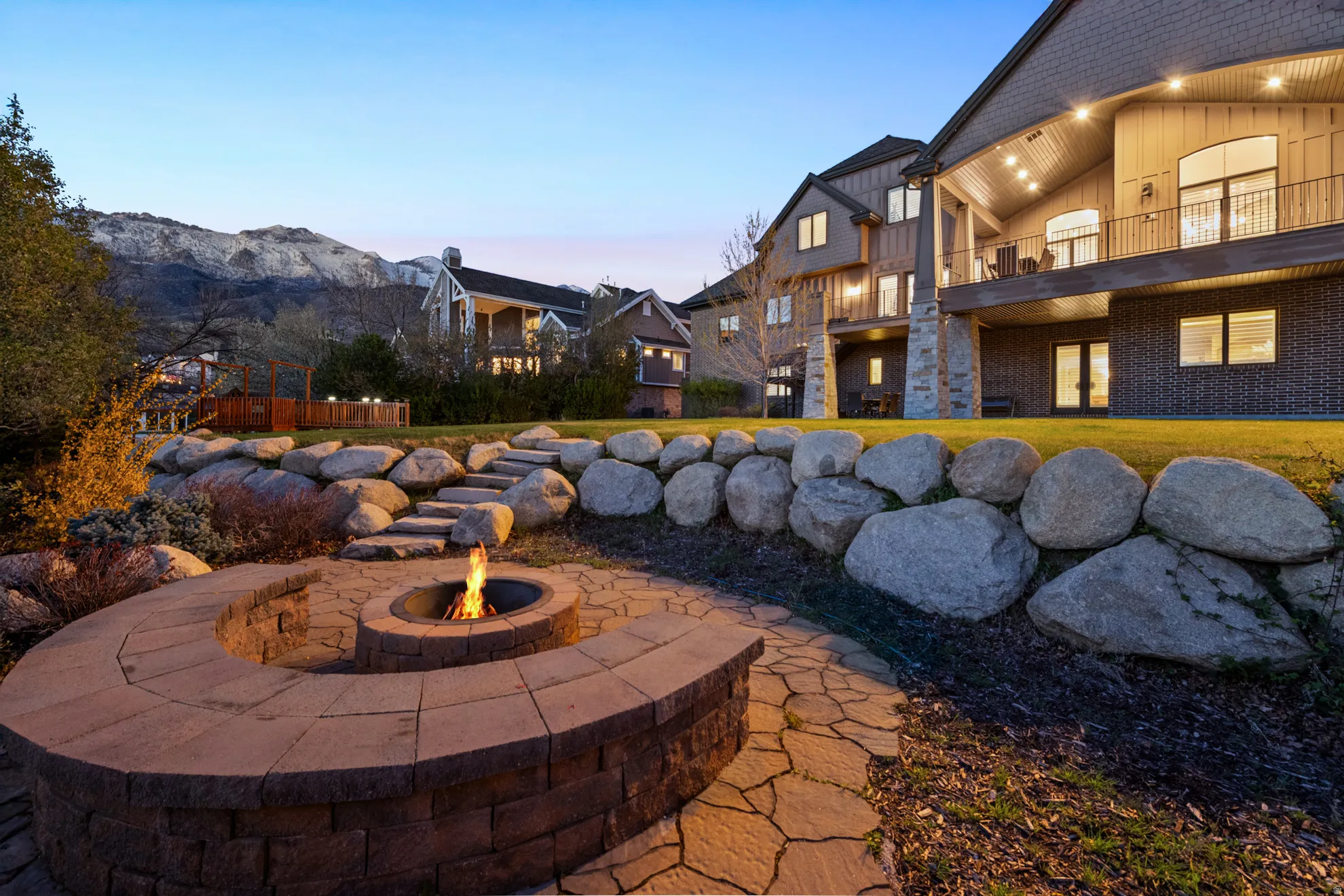 Expansive backyard featuring a built-in stone fire pit with curved seating, flagstone pathway, and rock retaining walls