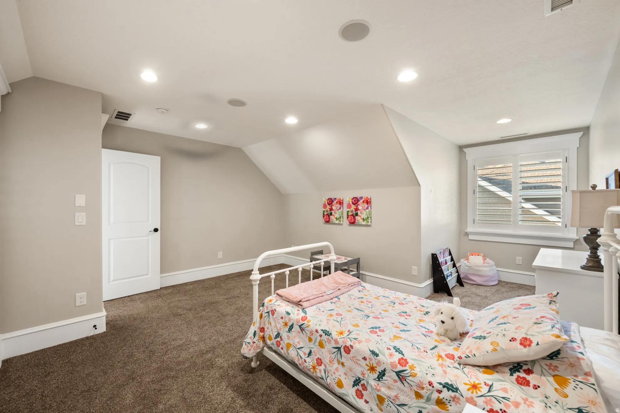 Carpeted interior room featuring a white paneled door, recessed ceiling lighting, and a window with plantation shutters