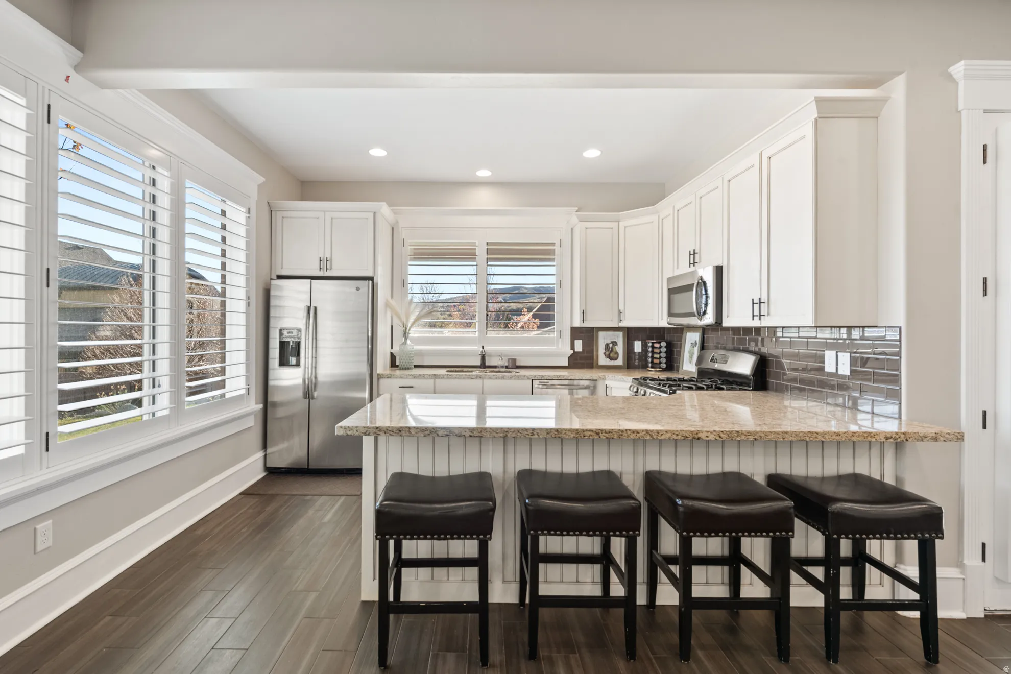 Open-concept kitchen featuring white shaker-style cabinetry, stainless steel appliances, and a breakfast bar with a light-toned countertop