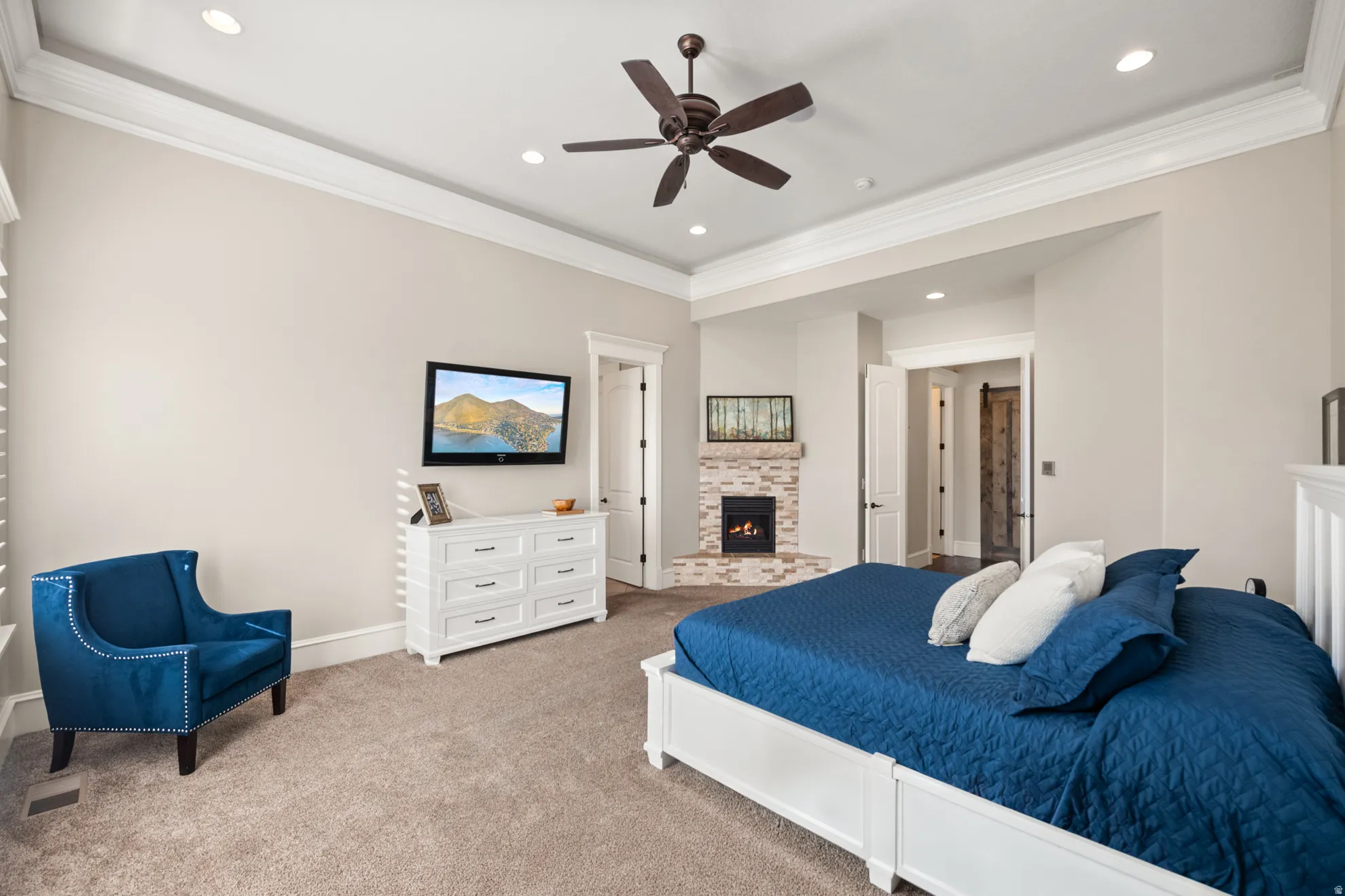 Spacious room featuring tray ceiling with recessed lighting and a ceiling fan, a corner fireplace with stacked stone surround, and carpet flooring