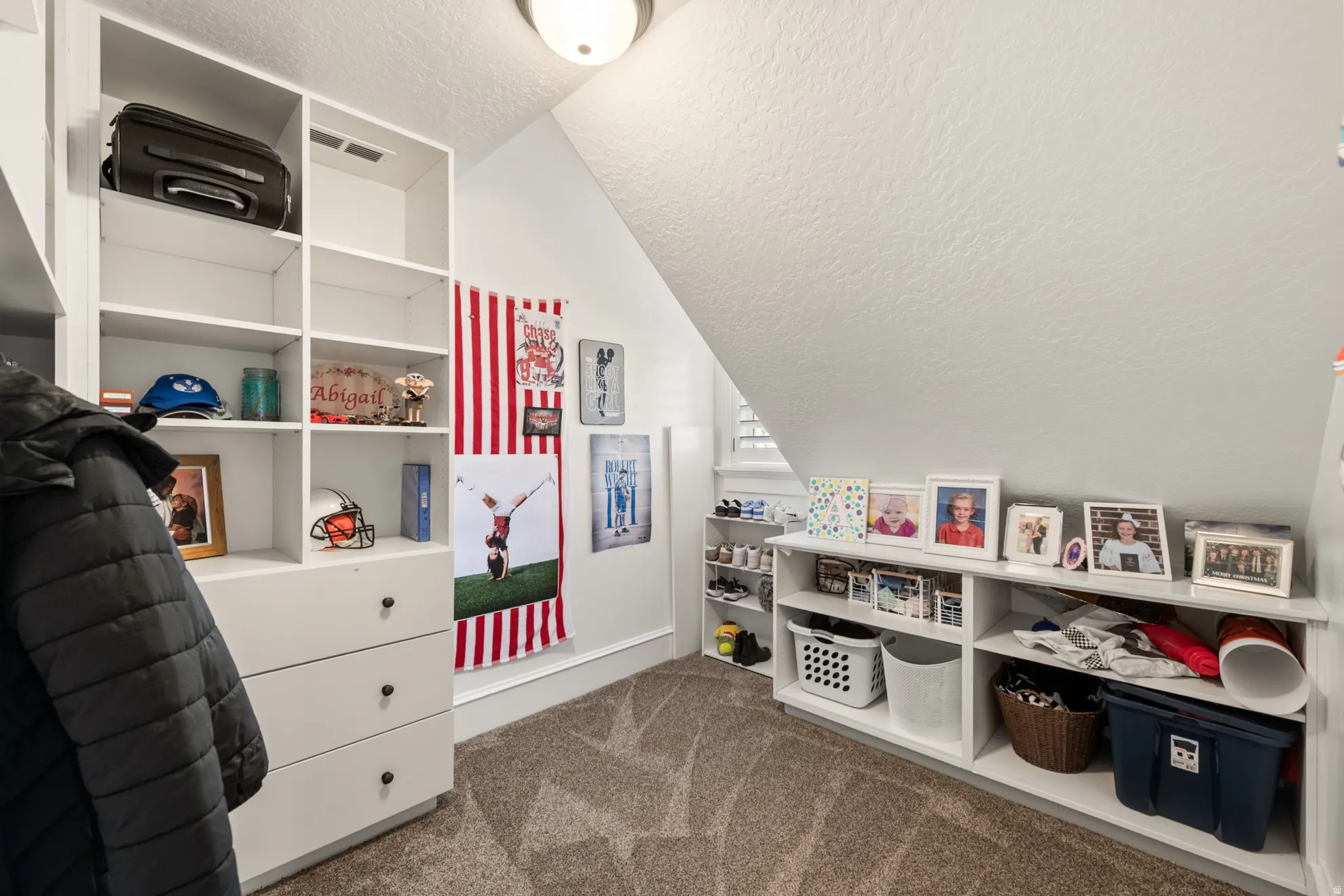 Carpeted bonus room featuring built-in white shelving, integrated drawers with dark hardware, and a window with white shutters