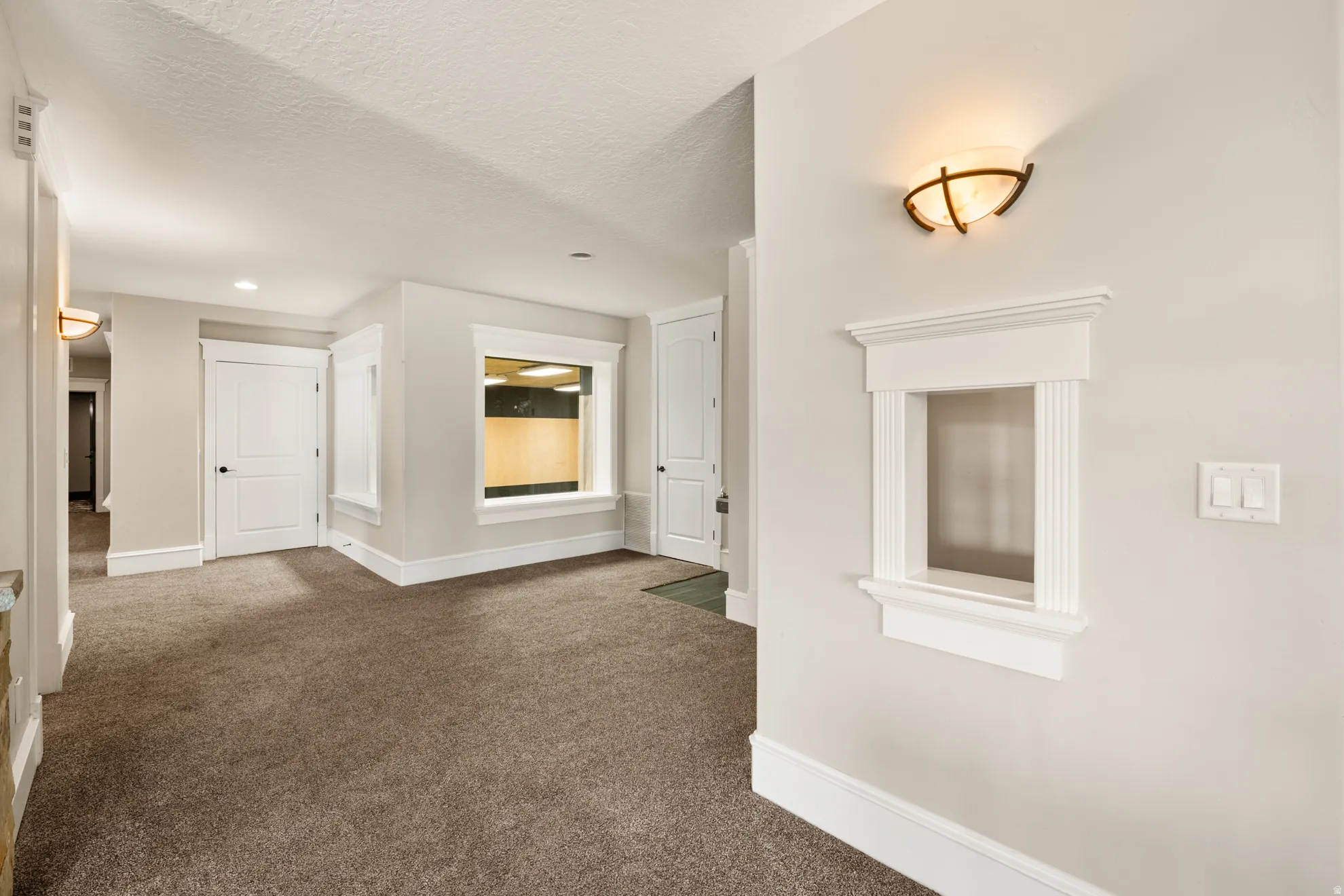 Interior wall with decorative pass-through window, sconce lighting, and light-toned carpet flooring