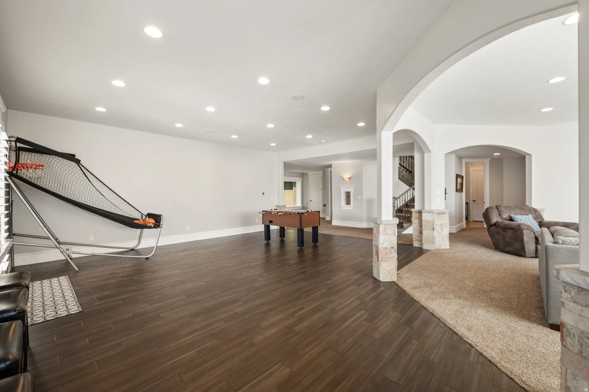 Spacious lower level featuring wood-finish flooring, recessed lighting, arched doorways, and stone-clad columns