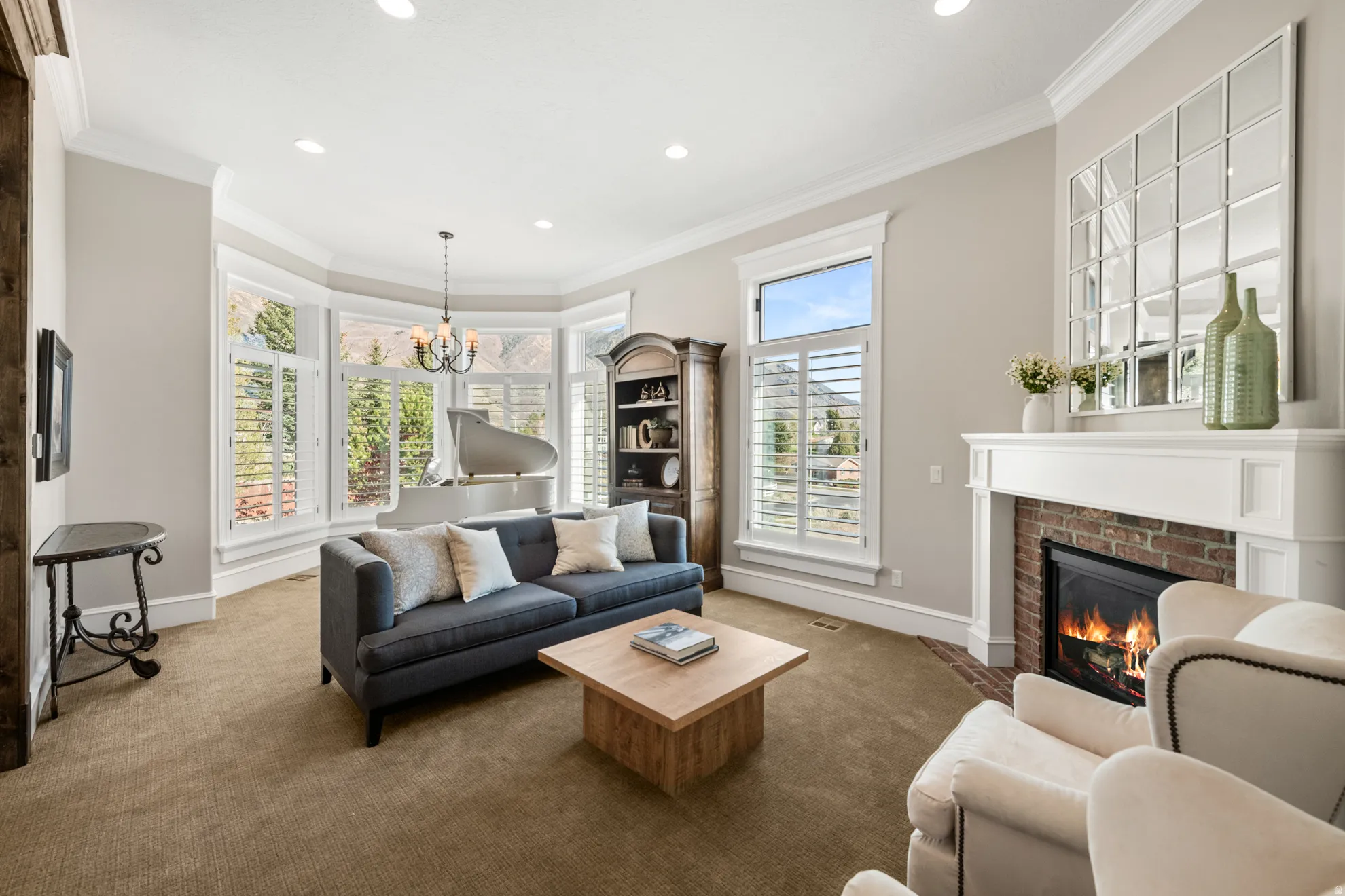 Living area featuring a brick fireplace with a white mantel, bay windows with plantation shutters, crown molding, and recessed lighting
