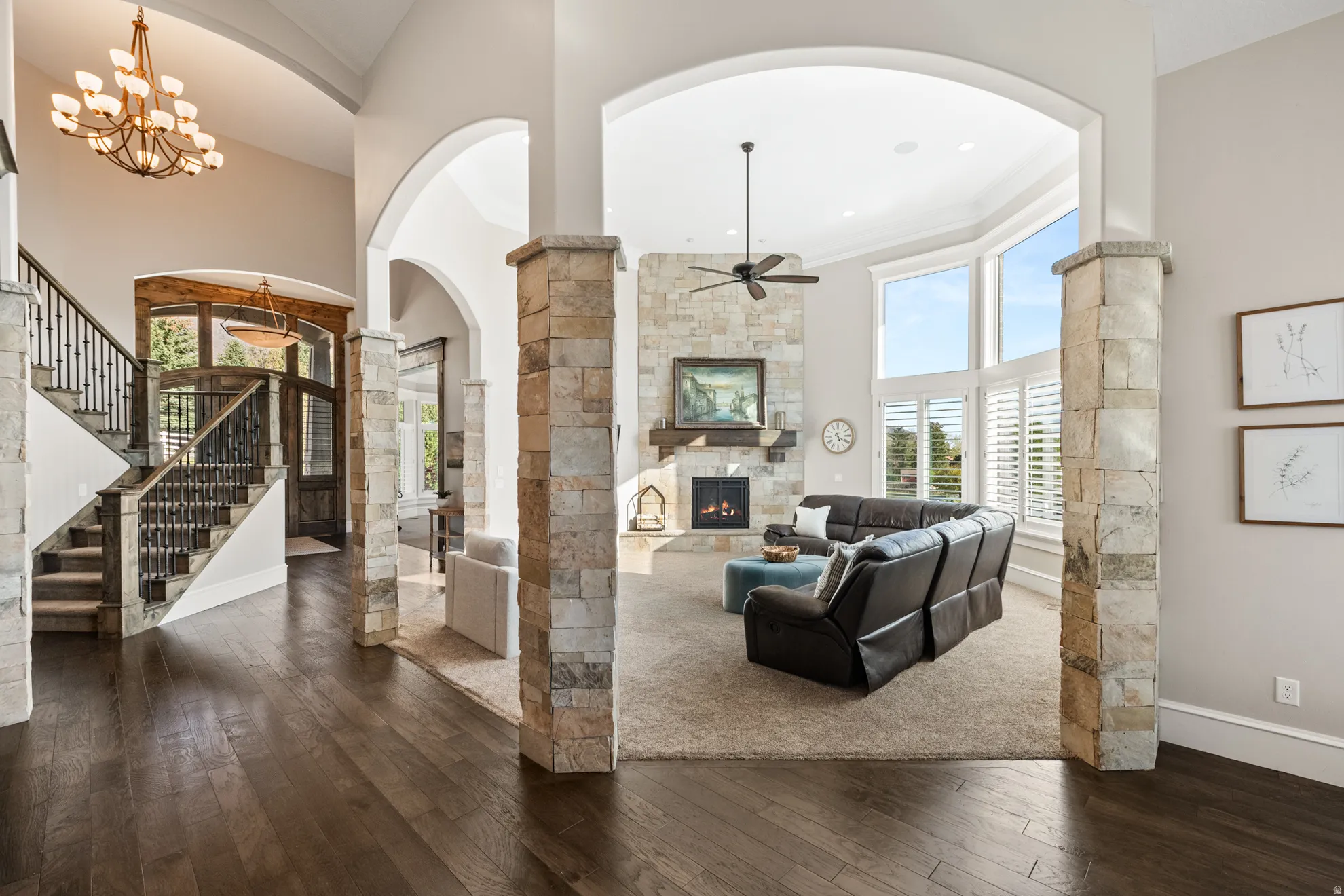 Expansive living area with wood-finish flooring, stone-clad archways, and a multi-level staircase with wrought iron balusters