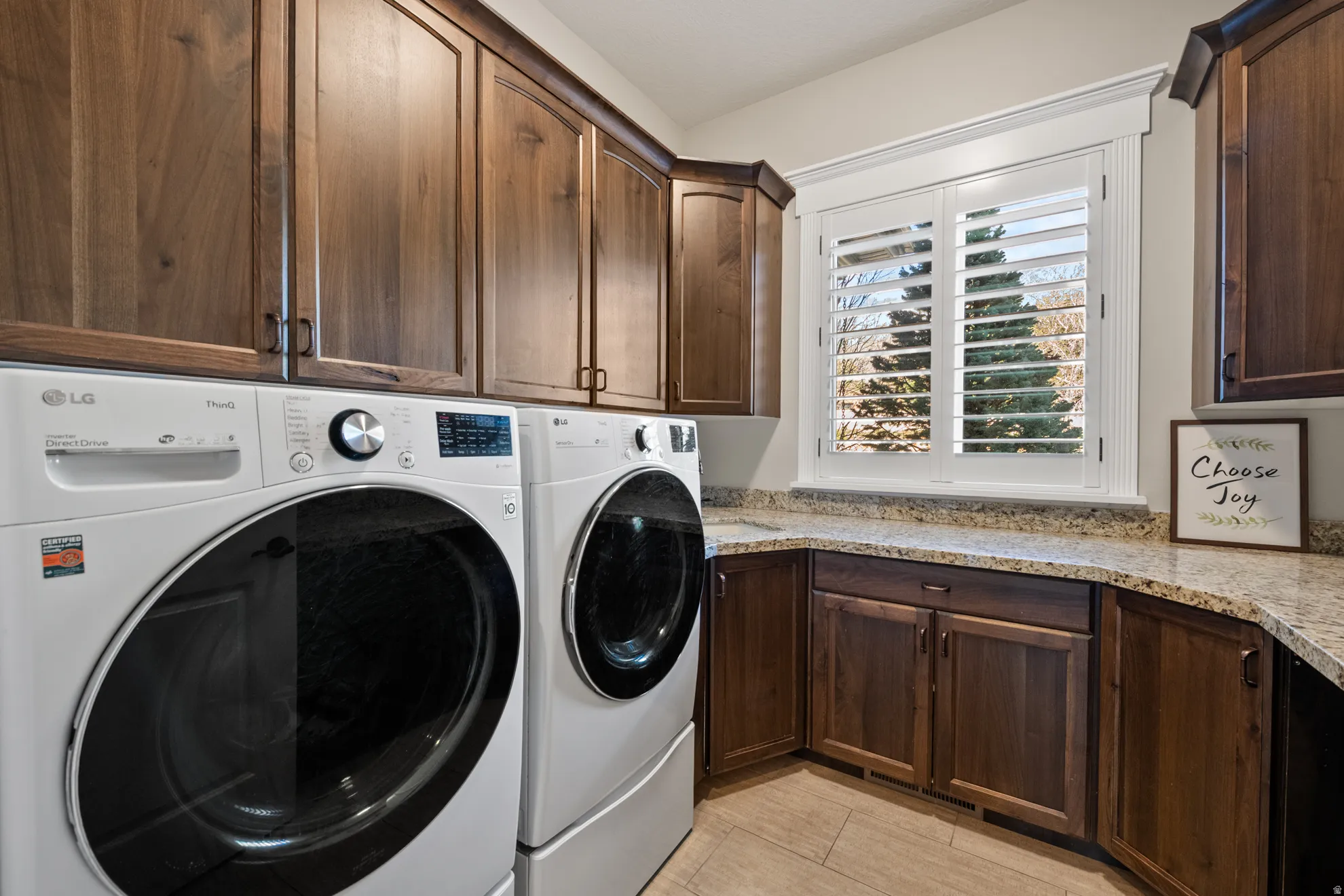 Laundry area featuring wood-finish cabinetry, granite-style countertops, and a window with plantation shutters