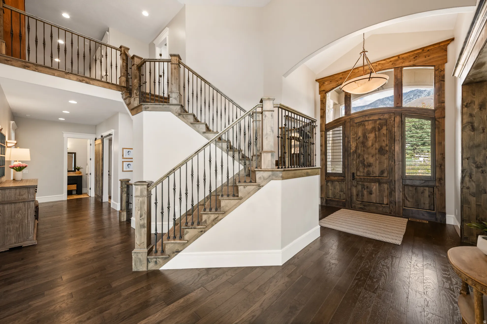 Grand foyer featuring dark wood-finish flooring, a double-height ceiling, and a prominent staircase with wrought iron balusters