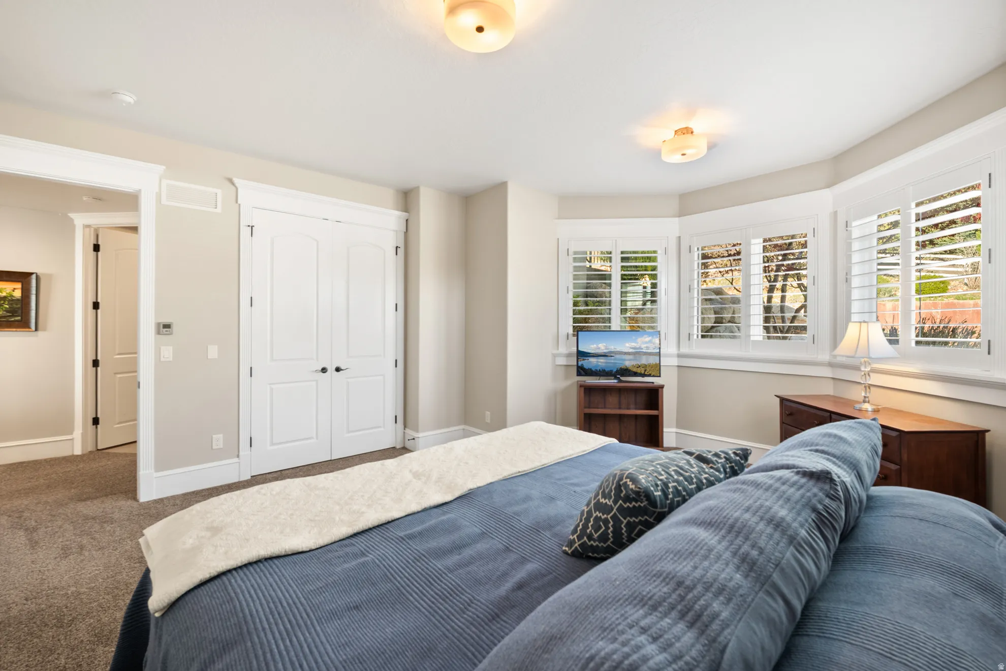 Carpeted room featuring a bay window with plantation shutters, double closet doors, and recessed ceiling lighting