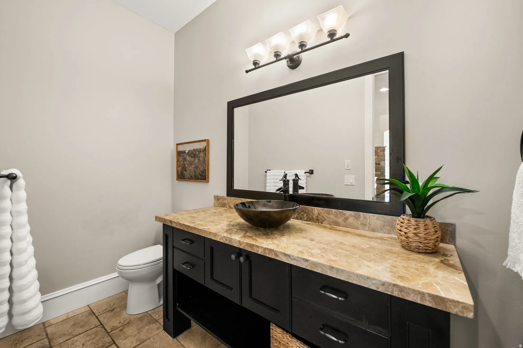 Powder room featuring a dark wood vanity with a vessel sink, a light-toned stone countertop, and a large framed mirror