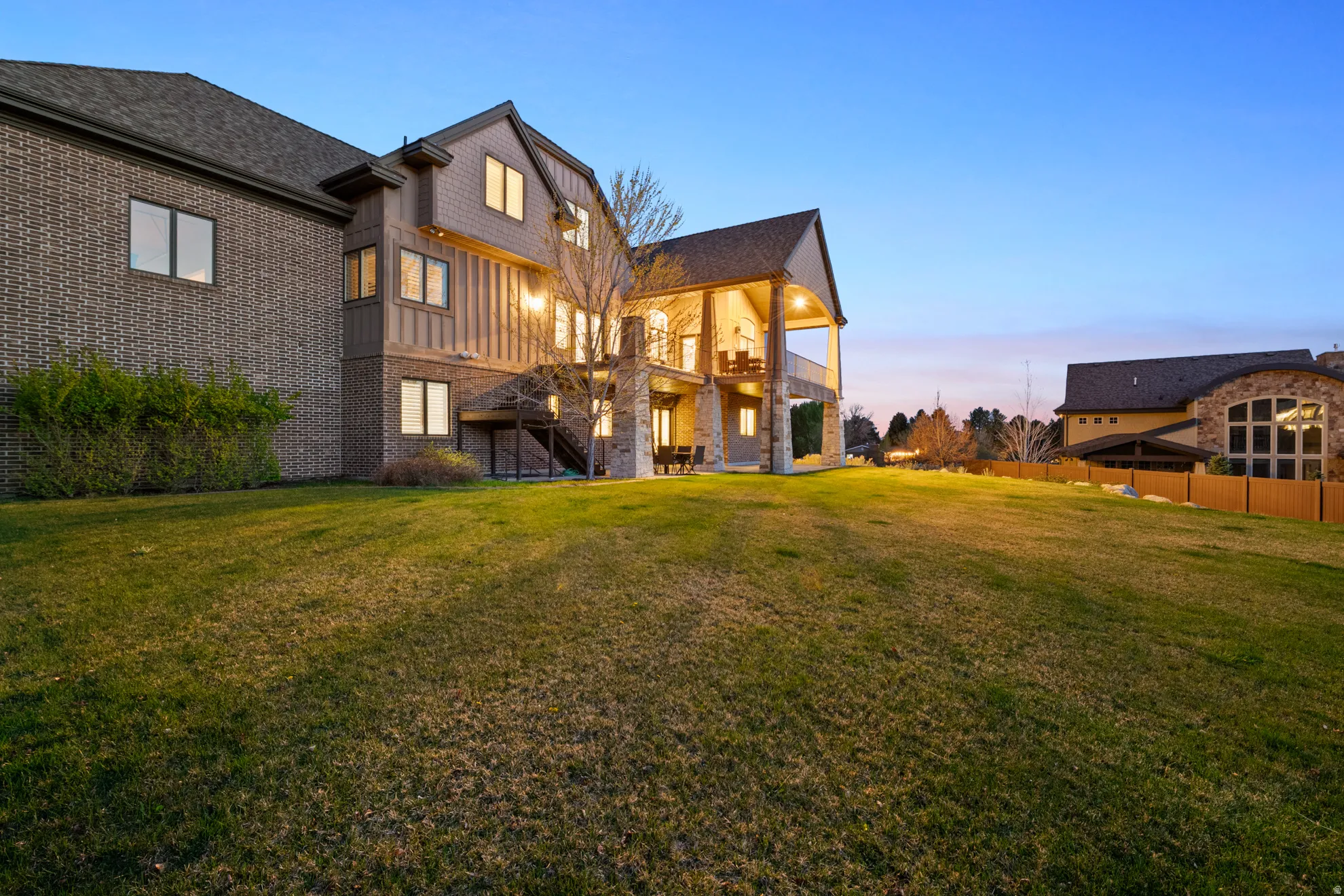 Expansive rear facade featuring brick and vertical siding, multiple windows, a covered patio, and an upper-level covered balcony