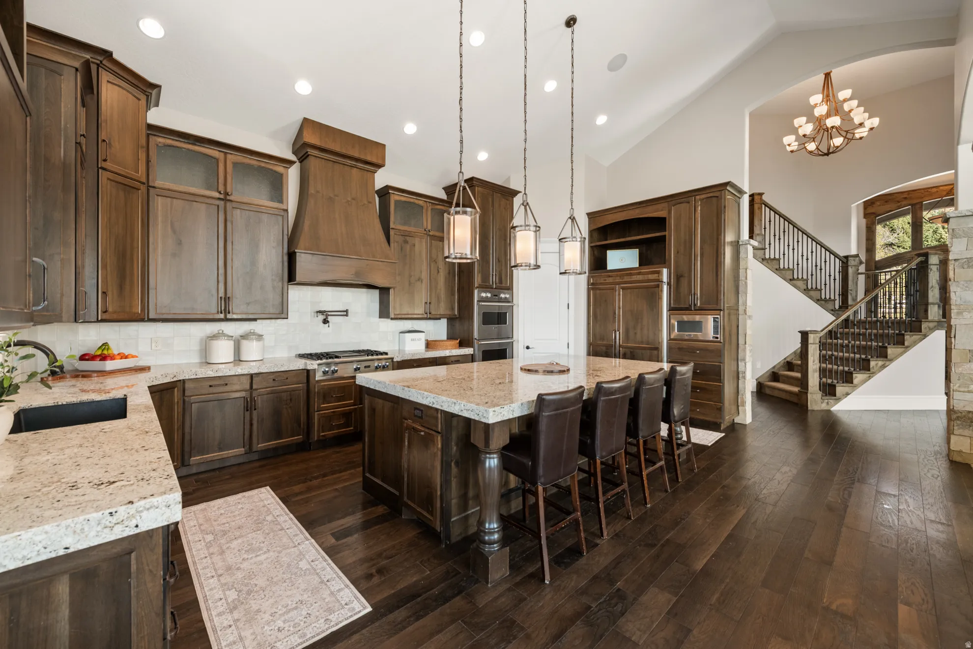 Gourmet kitchen featuring a large central island with seating, dark wood-finish cabinetry, light-colored countertops, stainless steel appliances, and a tile backsplash