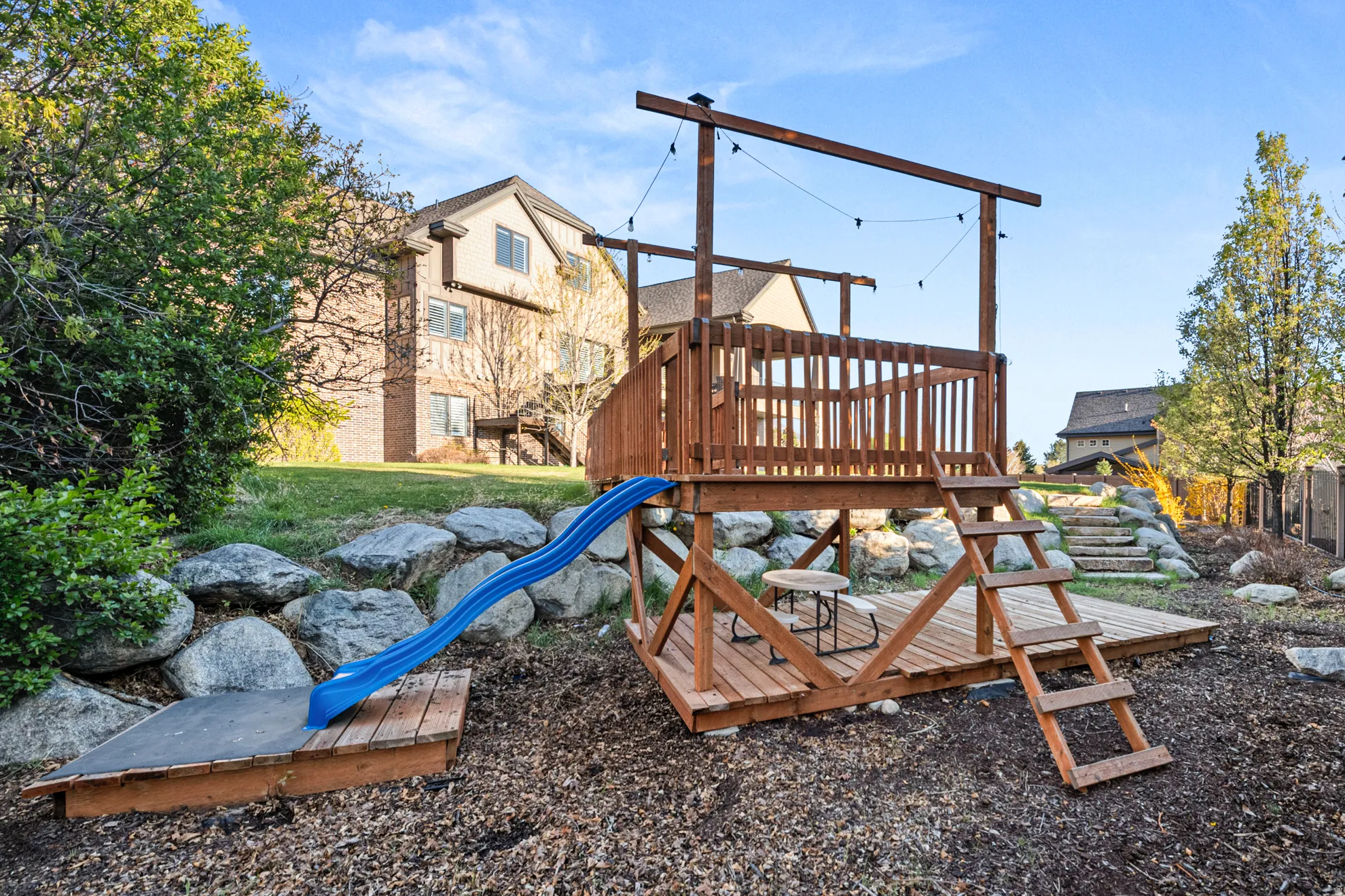 Multi-level wooden play structure featuring a slide and sandpit