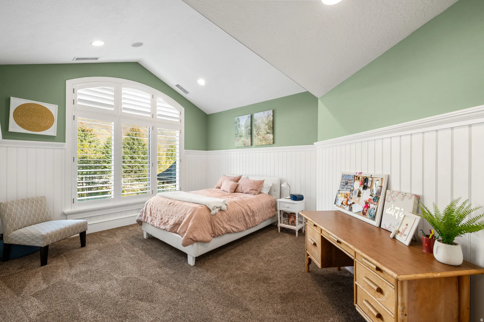 Spacious room featuring vaulted ceilings, recessed lighting, arched window with plantation shutters, wainscoting, and carpeted flooring
