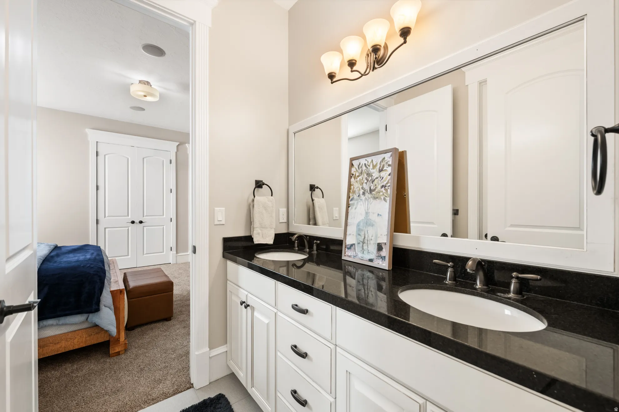 Dual vanity featuring a dark countertop, white cabinetry with dark hardware, and two undermount sinks