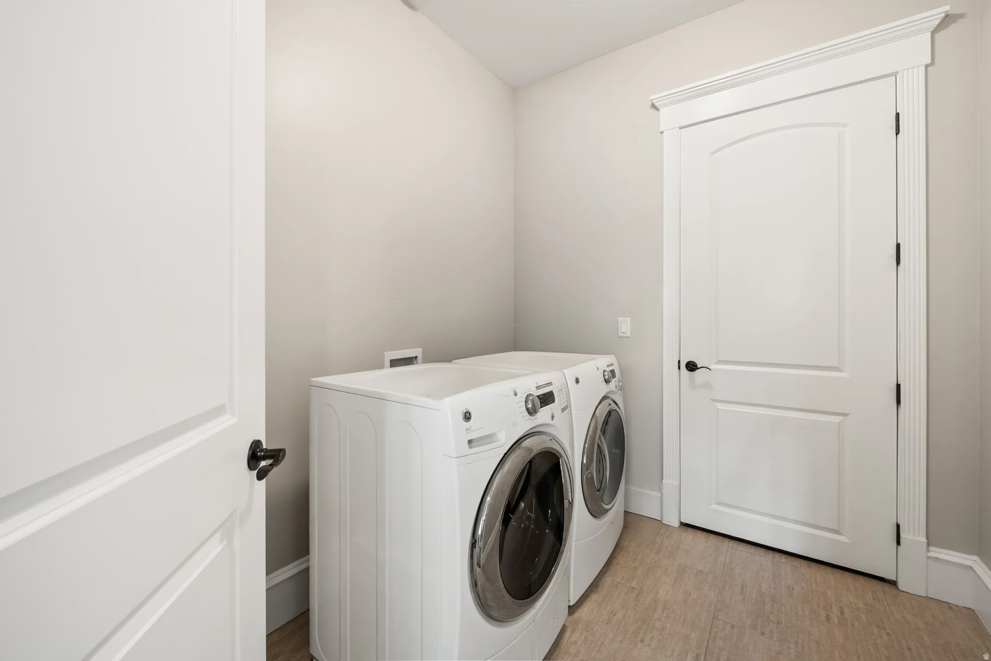 Dedicated laundry space featuring neutral wall tones, durable wood-finish flooring, and white trim work