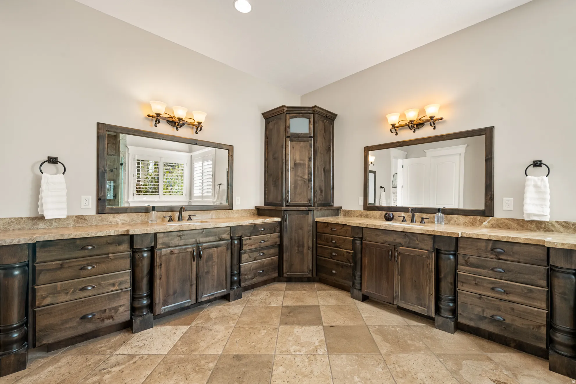 Dual vanity with stone countertops and wood-finish cabinetry, featuring a corner built-in storage unit