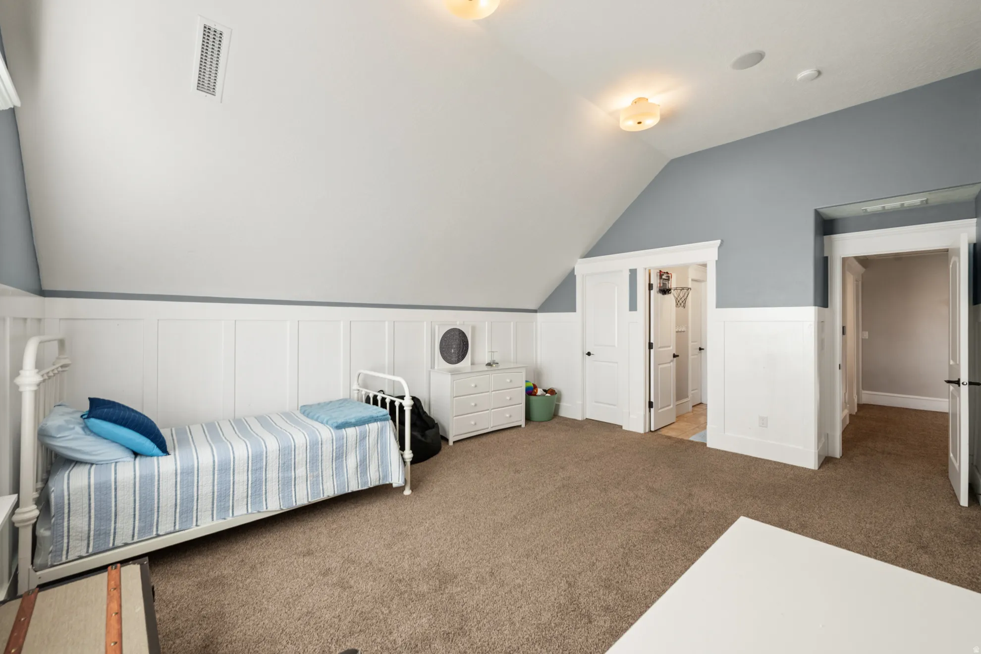 Room featuring textured carpeting, wainscoting, and a sloped ceiling