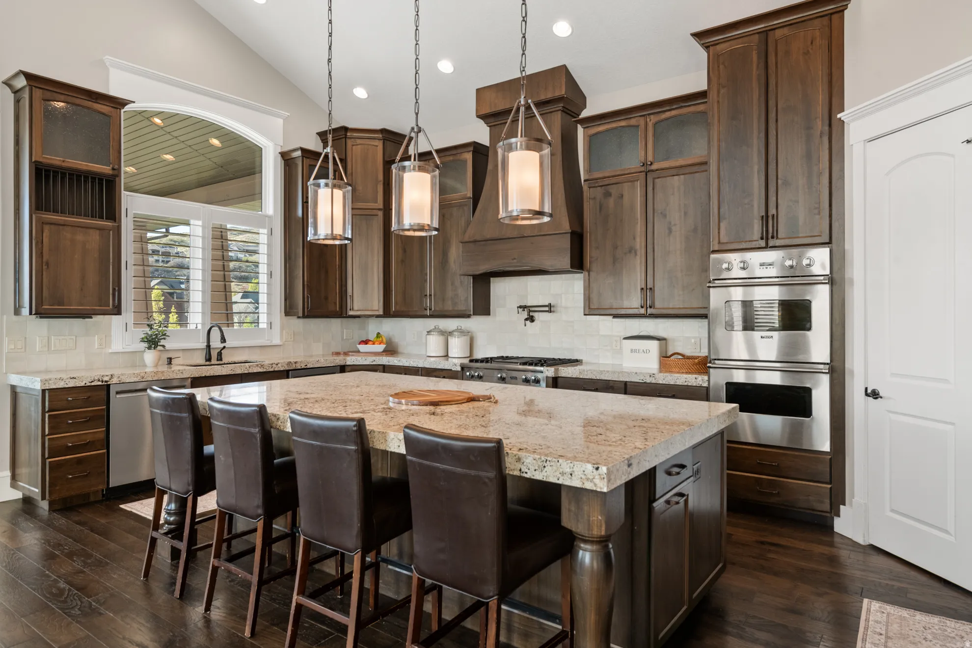 Gourmet kitchen featuring a large central island with seating, dark wood cabinetry, stainless steel double ovens, and wood-finish flooring