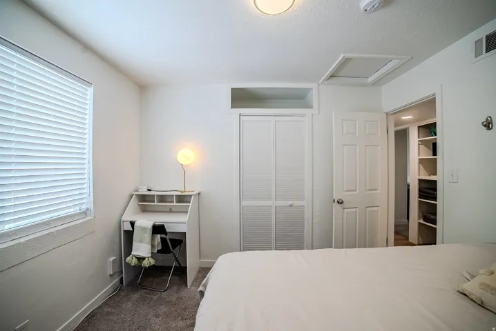 Bedroom featuring white walls, textured carpeting, and a window with blinds