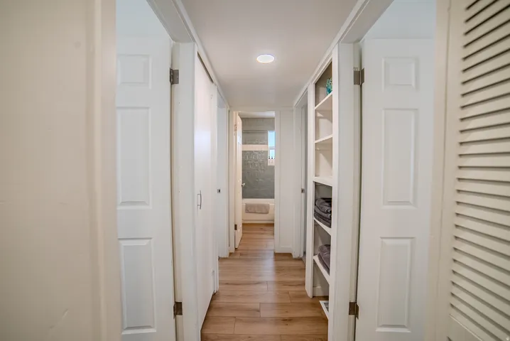 Hallway featuring wood-finish flooring, recessed lighting, white paneled doors, and a built-in shelving unit