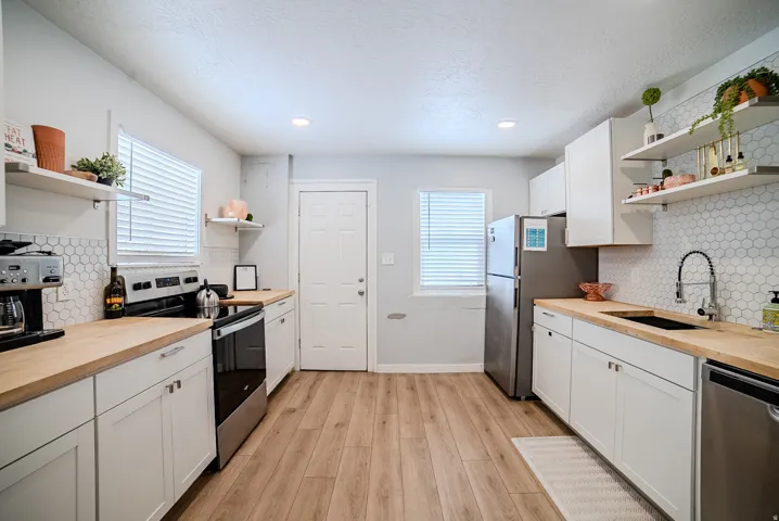 Kitchen featuring white shaker-style cabinetry, wood-finish countertops, hexagon tile backsplash, stainless steel appliances, and wood-finish flooring