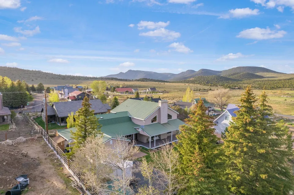 Property featuring a green metal roof, a covered wrap-around porch, multiple mature evergreen trees, and a mountain backdrop