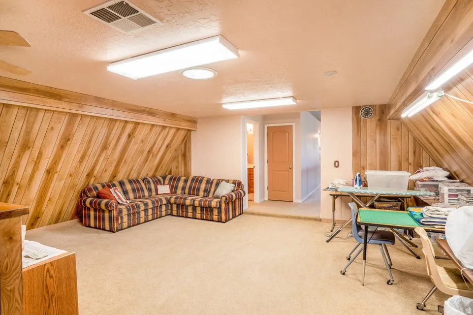 Spacious room featuring sloped ceilings, wood-paneled walls, and soft carpeting