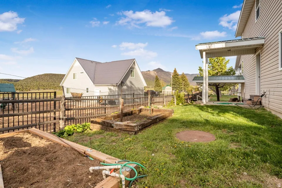 Expansive backyard featuring a covered patio, raised garden beds, a fenced perimeter, and distant mountain scenery