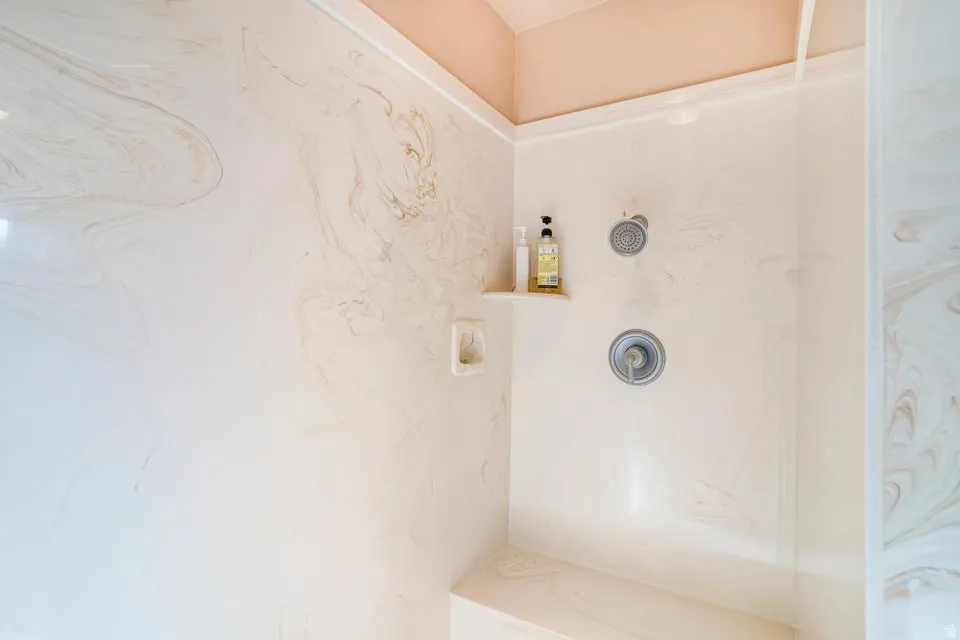 Shower enclosure featuring a built-in bench, integrated shelving, and a chrome shower head with a separate handle