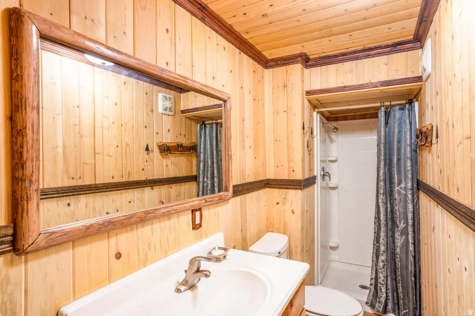 Bathroom featuring light-toned wood paneling, dark wood trim, a white vanity with integrated sink, a large mirror with a rustic wood frame, and a stand-up shower with white surround