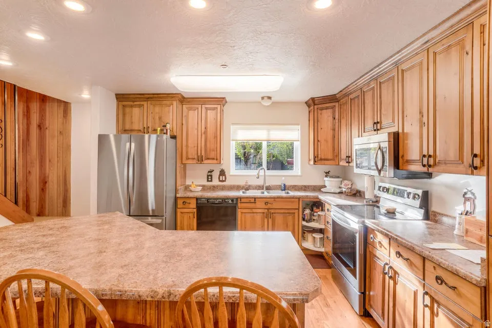 Kitchen featuring wood-finish cabinetry, stainless steel appliances, a composite countertop, an island with breakfast bar seating, and a stainless steel sink with a single-handle faucet