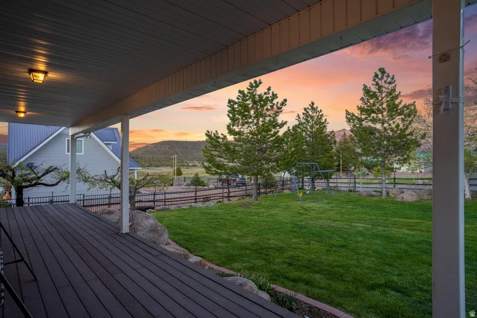 Expansive covered deck with dark wood-finish flooring extending to a lush green lawn