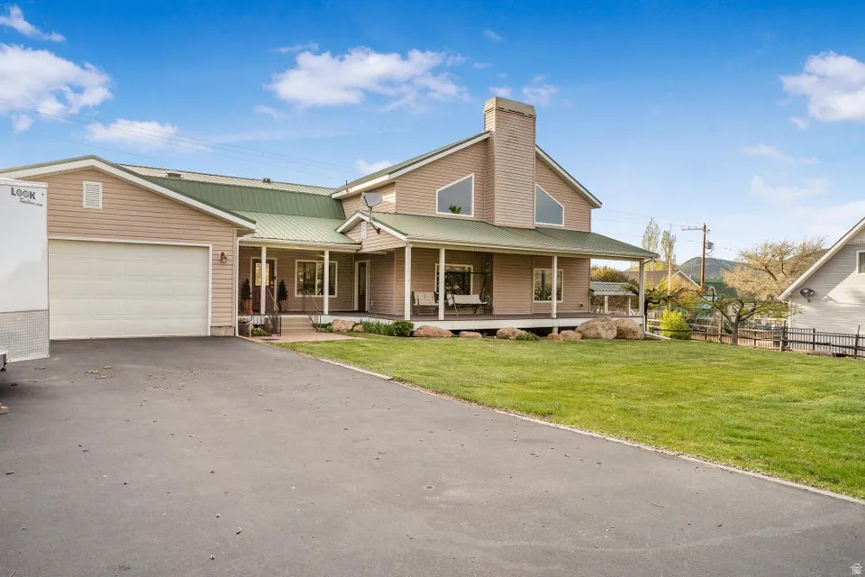 Exterior featuring a green metal roof, light-colored siding, a covered porch, an attached garage, and a paved driveway