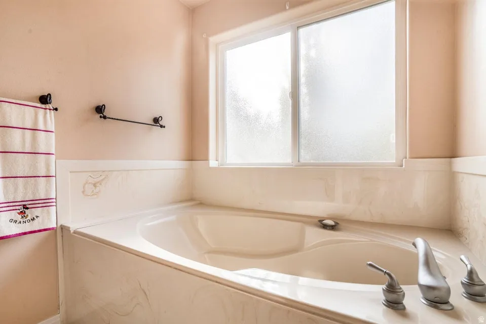 Built-in soaking tub with brushed nickel fixtures, surrounded by a marbled enclosure and wainscoting