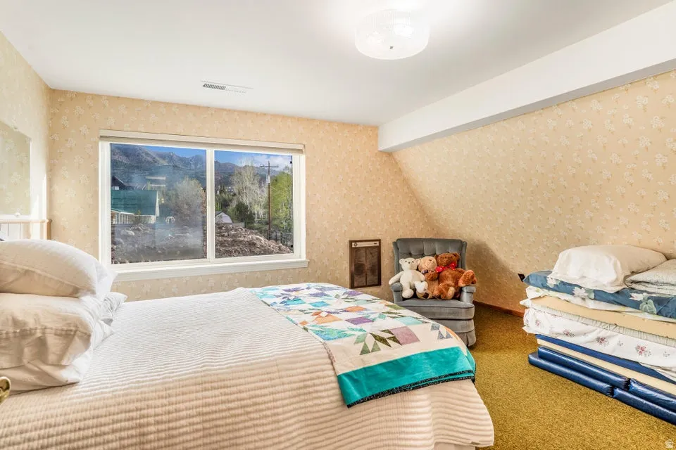 Bedroom featuring a large window, patterned wallpaper, textured carpet, and a ceiling-mounted light fixture