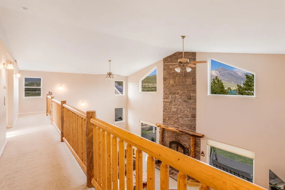 Upper-level hallway overlooking a great room with a stone fireplace, exposed wood mantel, and ceiling fan