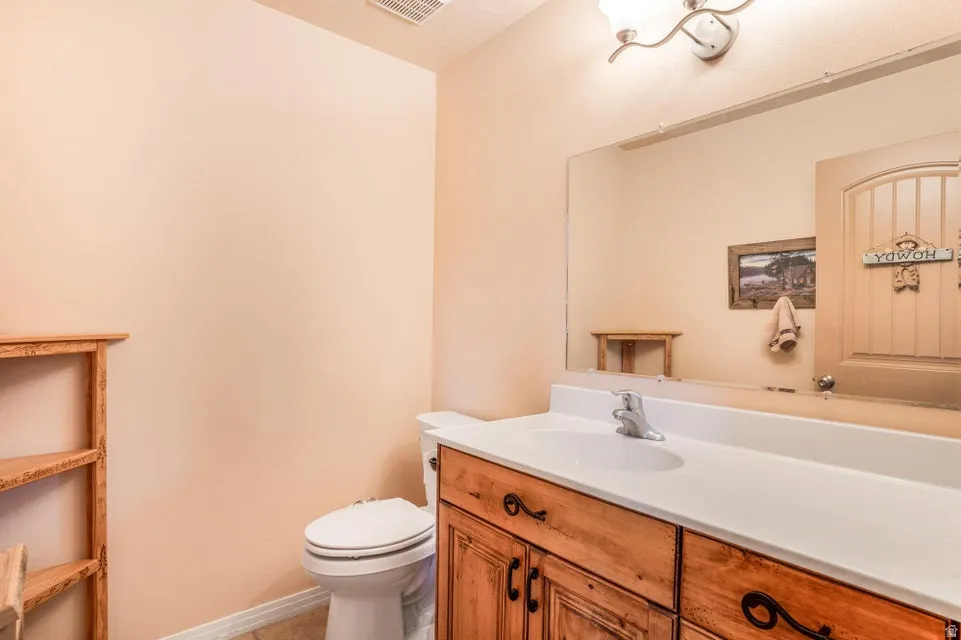 Bathroom featuring a wood-finish vanity with a white countertop and integrated sink, a toilet, and a wall-mounted light fixture