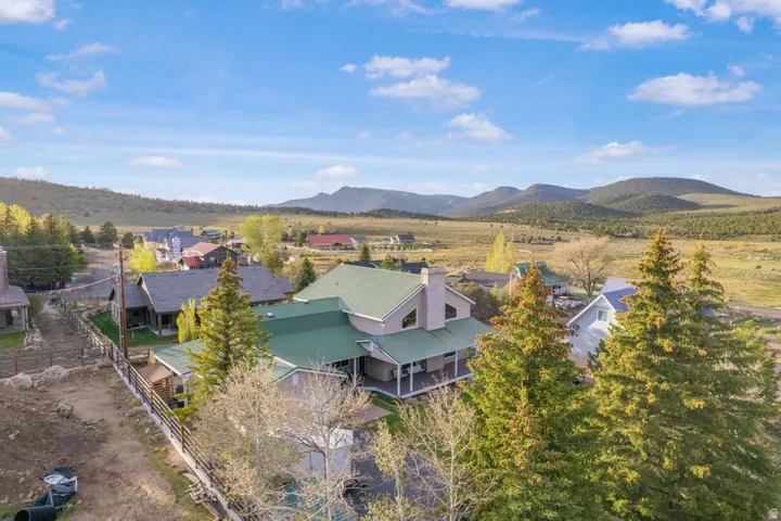 Property featuring a green metal roof, a covered wrap-around porch, multiple mature evergreen trees, and a mountain backdrop