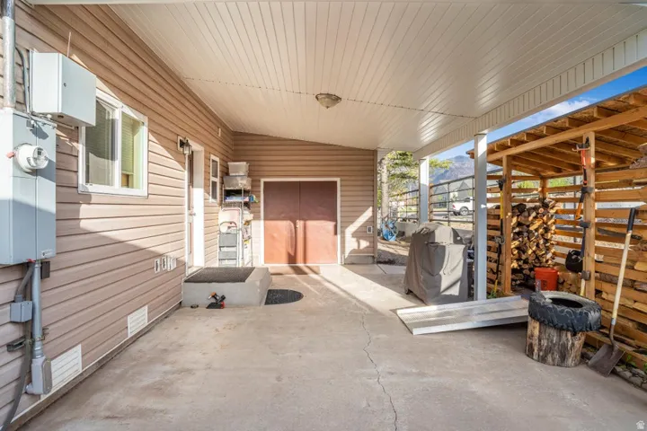 Covered concrete patio extending from the tan vinyl-sided structure, featuring a white soffit ceiling