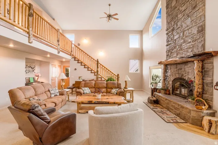 Great room featuring a vaulted ceiling, stone-clad fireplace with wood mantle, lofted walkway, and a rustic wood staircase