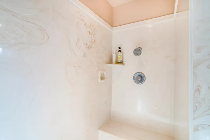 Shower enclosure featuring a built-in bench, integrated shelving, and a chrome shower head with a separate handle