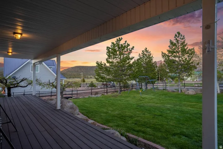 Expansive covered deck with dark wood-finish flooring extending to a lush green lawn