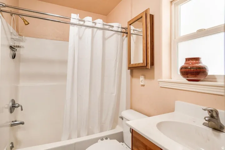 Bathroom featuring a white bathtub with chrome fixtures and shower curtain rod, a wood-finish medicine cabinet, and a white vanity with an integrated sink and chrome faucet